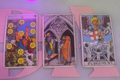 Three tarot cards displayed on a stand with a neon sign in the background.